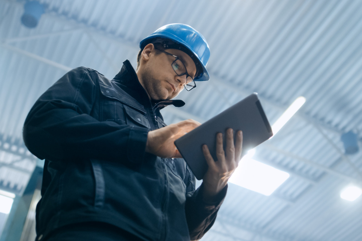 Factory worker in a hard hat is using a tablet computer.